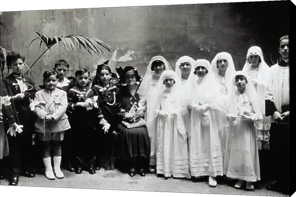 Portrait of a group of children in first communion dress. A lady and an altar boy are posing next to the children