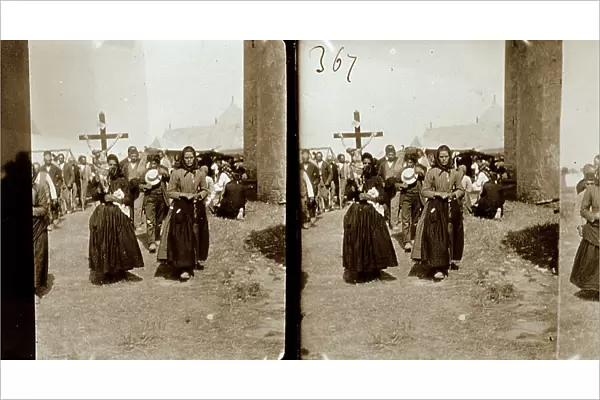 Religious procession along the streets of a village. One of the women in the foreground is carrying a cross