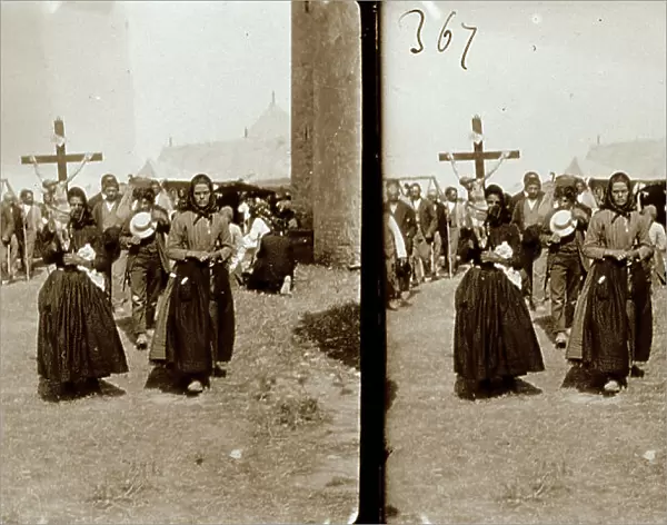 Religious procession along the streets of a village. One of the women in the foreground is carrying a cross