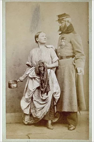 Studio portrait of a Russian soldier next to a woman dressed in simple work clothes. The woman holds a small pot in her right hand. The man rests one hand on her shoulder