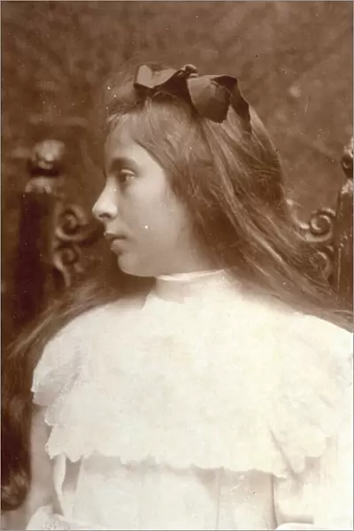 Profile of a little girl in formal dress, with frills and lace. Her long hair falls over her shoulders and is decorated with a bow