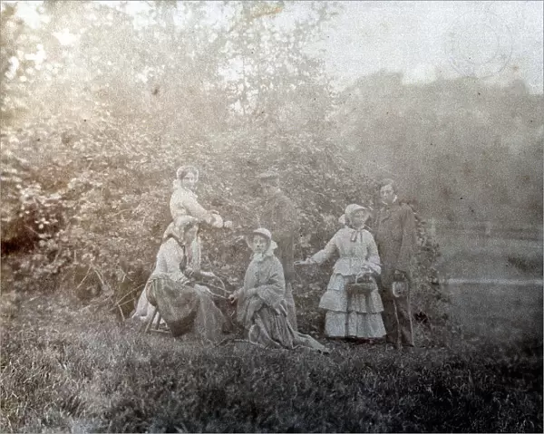 Group of men and women in a field. One of the ladies is sitting while another one is kneeling in front of her. Behind them, standing, the other figures