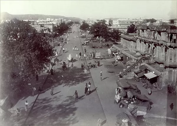 Panoramic view of the indian city of Jaypur. In the foreground there is a long avenue full of passers by, animals and street venders