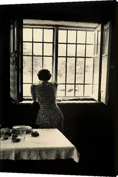 Woman looking out the window; in the foreground, a set table