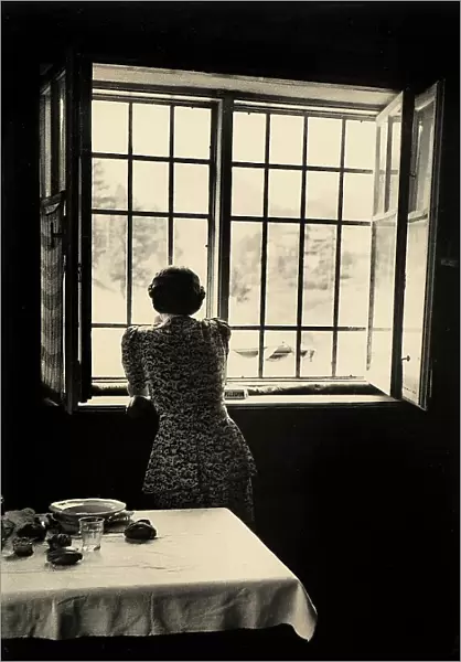 Woman looking out the window; in the foreground, a set table