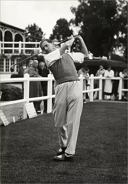 The captain F. Francis takes a shot at a golf tournament; in the background, spectators
