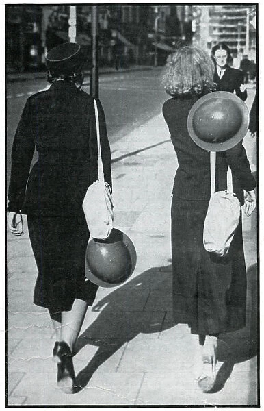 Backs of two walking girls holding helmets, September 1939