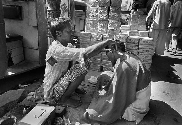 A barber squats in the street in Chandni Chouk, Old Delhi