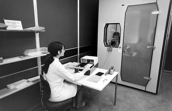 Biomedical centre, London -- a woman operates a machine while a patient in a locked room