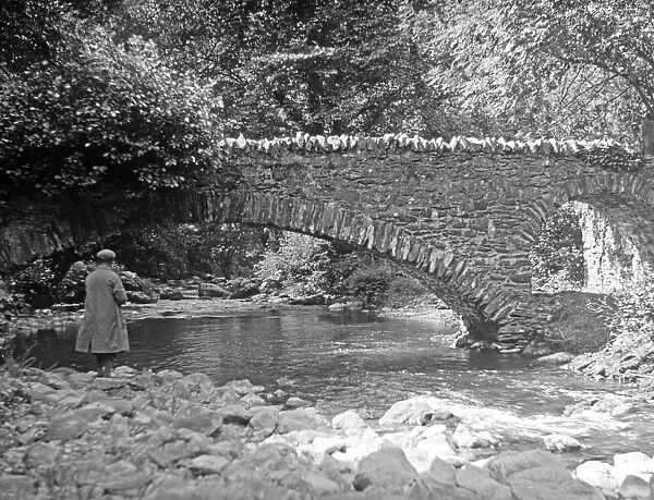Man standing by a stream near a bridge