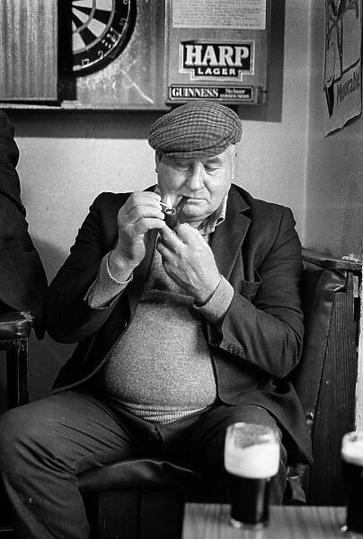 Mature man wearing cloth cap lights his pipe in an Irish pub