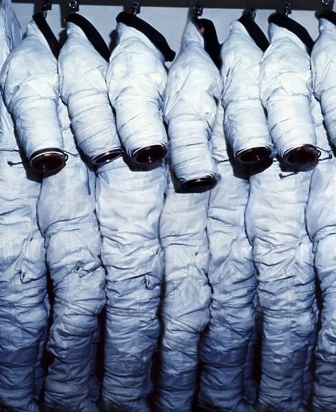 Space suits hanging in a row from hooks. These space suits