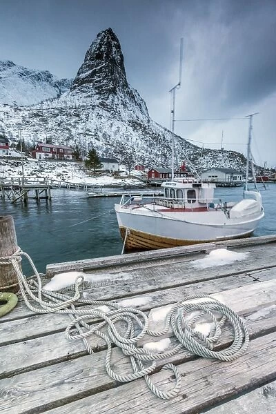 A boat moored in the cold sea in the background the snowy peaks, Reine. Lofoten Islands
