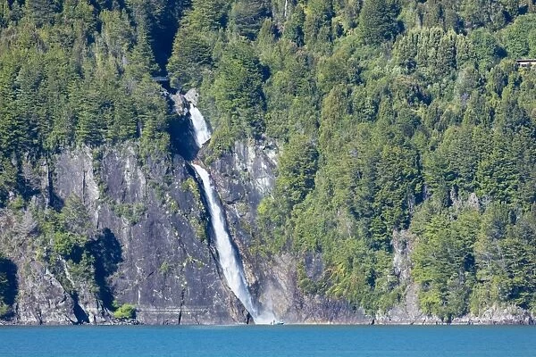 A boat in front of a waterfall on Puelo Lake in the Tagua Tagua reserve, Patagonia