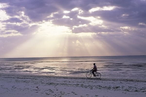 Fisherman cycling along the beach near Bweju against dramatic sky, island of Zanzibar