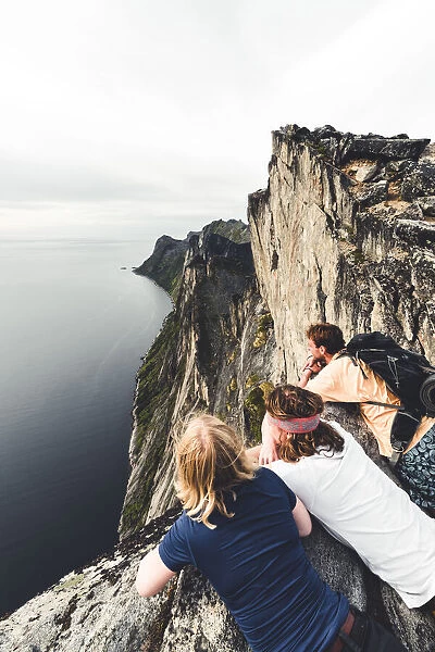 Three friends enjoying the view of the fjord leaning on rocks on Segla mountain peak