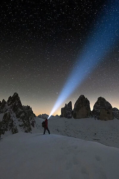 Hiker with head torch admiring stars on Monte Paterno and Tre Cime di Lavaredo