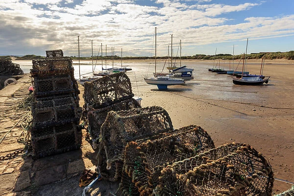 Lobster pots on harbour wall and yachts on beach at low tide on a summer evening