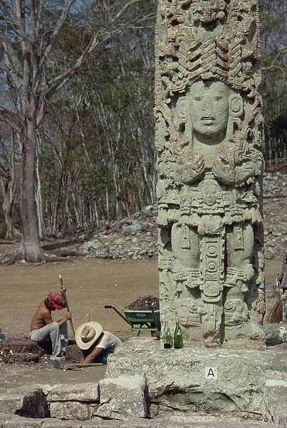 Two men excavating beside the Main Court Stela in the