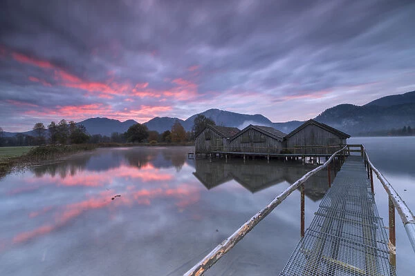 Purple sky at sunset and wooden huts are reflected in the clear water of Kochelsee