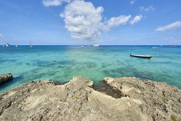 Rocky coastline in Cayman Islands with fishing boat in the transparent blue water