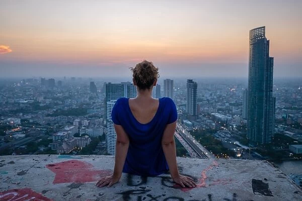 A single woman watching sun set over city skyline at dusk, Bangkok, Thailand, Southeast Asia