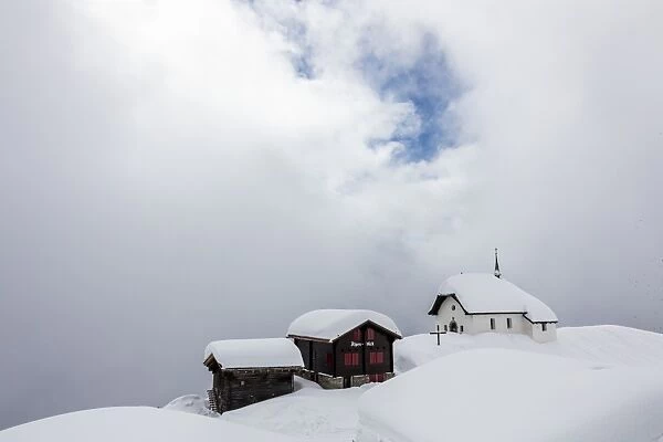 Snow covered mountain huts and church surrounded by low clouds, Bettmeralp, district of Raron