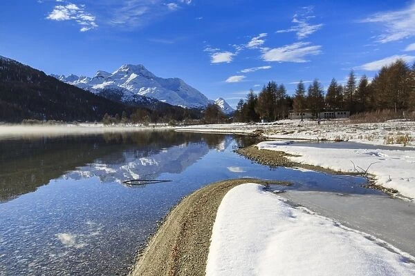 Snowy peaks are reflected in Lake Silvaplana still partially frozen, Maloja, Canton of Graubunden