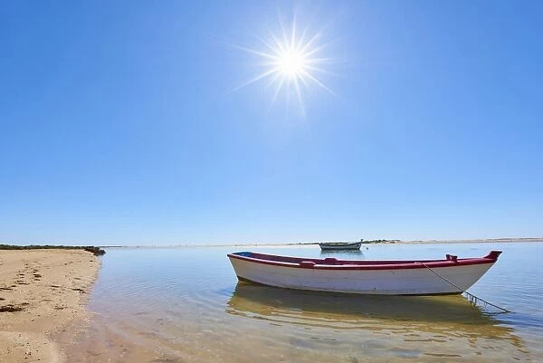 The sun shines above a small fishing boat on transparent lagoon water in Cacela Velha
