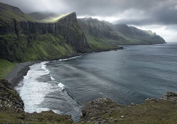 View over a hidden bay with the sun filtering through the clouds, Faroe Islands, Denmark