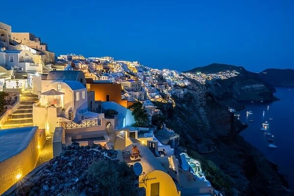 The view from Oia castle along Santorinis caldera during the evening blue hour with