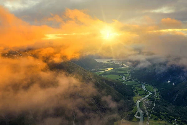 Aerial view of sun rays in the sunset sky lighting up the clouds over Romsdalen valley