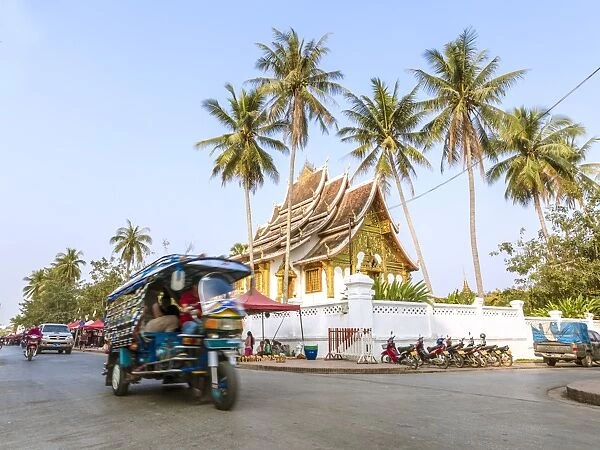 Laos, Luang Prabang. Street view with tuk tuk and Wat Mai temple in the background