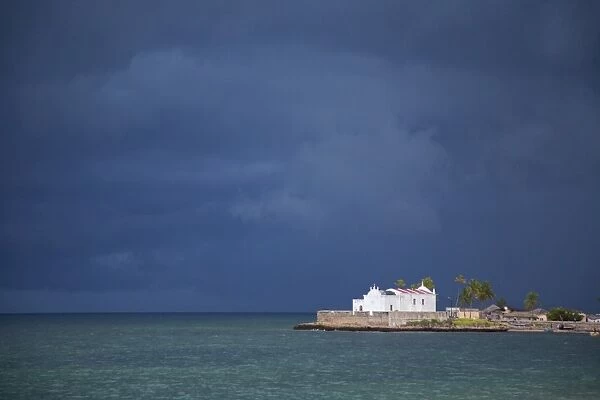 Mozambique, Ihla de Mozambique, Stone Town. The Church of Santo Antonio stands illuminated ahead of a dark approaching storm