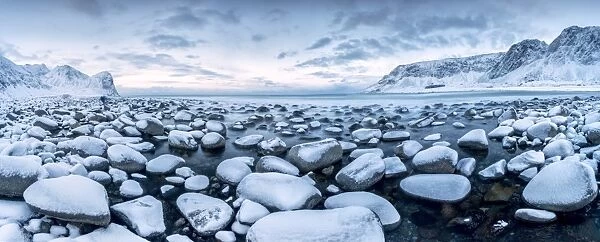 Rocks in the cold sea and snow capped mountains under the blue light of dusk Unstad
