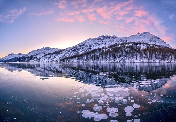 Sunrise on ice bubbles trapped in Lake Sils with Piz Da La Margna in background