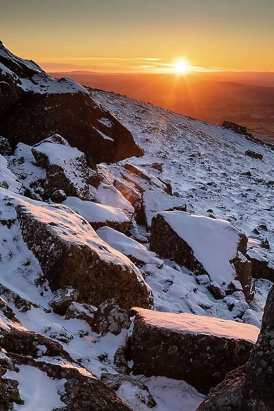 Sunset over snow covered rocks on Sourton Tor, Dartmoor National Park, Devon, England. Winter (December) 2022
