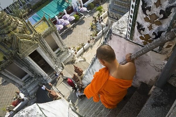 Thailand, Bangkok. A monk descends the steps of the prang (Khmer-style tower) at Wat Arun