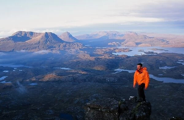 A mountaineer on Suilven summit at Dawn in Scotland UK looking towards Stac Polaidh and Cul Mhor