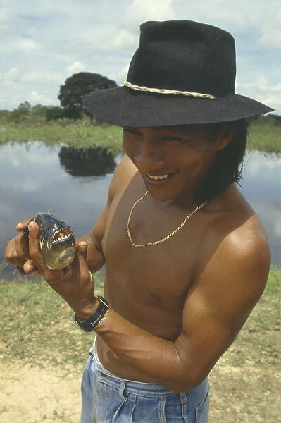10058198a. Brazil, Indian man wearing hat holding Piranha fish