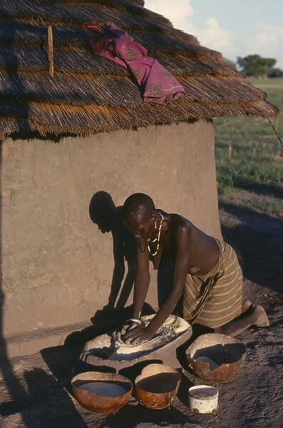 20050059. SUDAN Tribal People Dinka woman grinding dura outside hut casting shadow on wall
