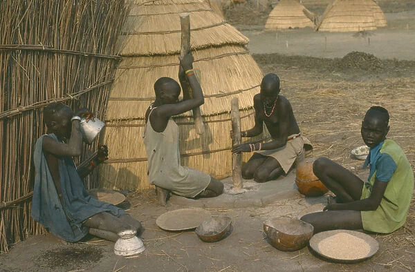 20073150. SUDAN Agriculture Dinka women pounding millet outside their hut