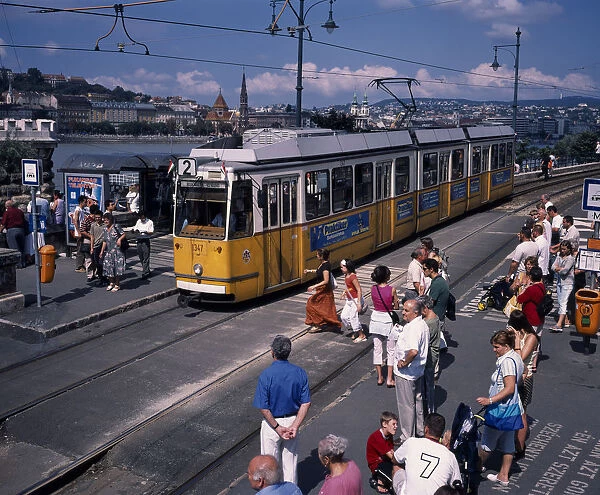 HUNGARY, Budapest Electric yellow tram and groups of people gathered at tram stop