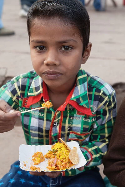 India, Uttar Pradesh, Varanasi, A boy eats a snack of bhel puri on the ghats