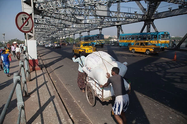 India, West Bengal, Kolkata, Men push a cart loaded with goods across Howrah Bridge
