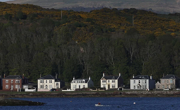 A boat passes houses in Millport, Scotland