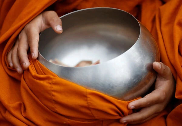 A Buddhist monk holding a vessel sits at the premises of Boudhanath Stupa while waiting