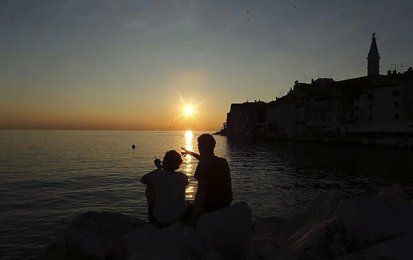 A couple watches the sunset during the first day of summer in the Adriatic town of Rovinj