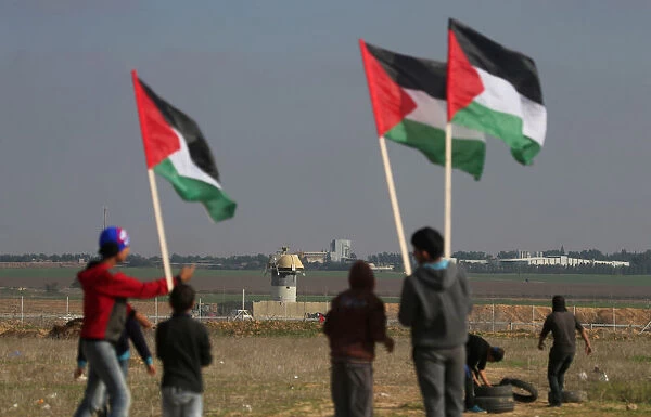 Demonstrators hold Palestinian flags during clashes with Israeli troops near the border