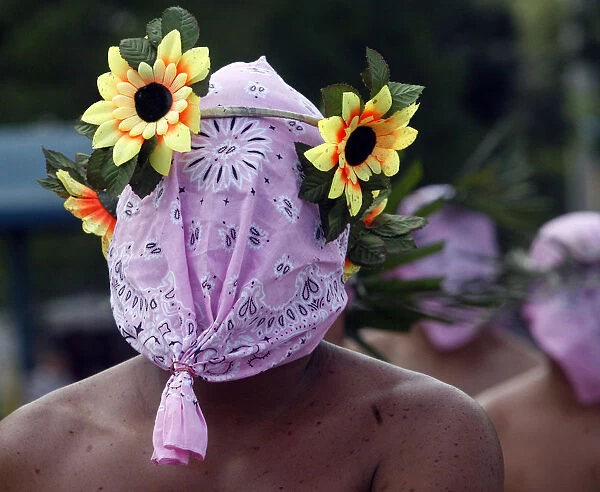 A hooded penitent wears an improvised crown made of plastic flowers during Maundy